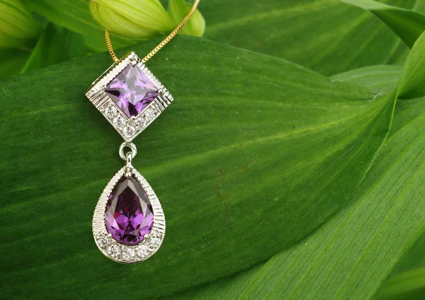 Jewellery pendant with diamonds and spinel on green leafs backgr