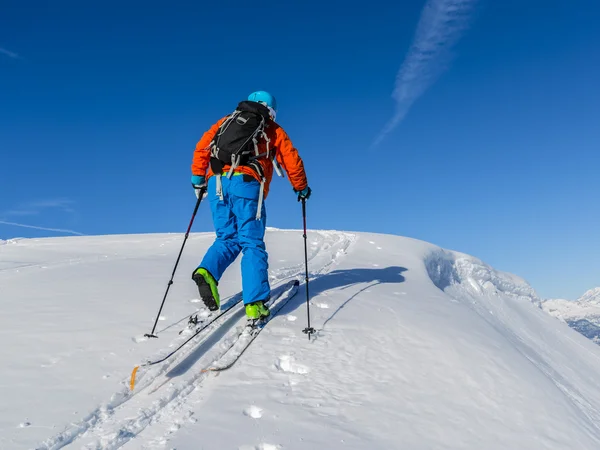 Ski touring man reaching the top at sunrise in Swiss Alps.