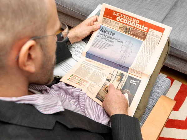 Man reading Le Figaro Economie French newspaper about prices of