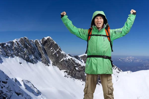 Happy male mountain climber with arms raised above the head. In the background the high mountains.