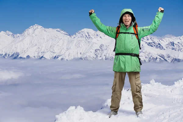 Happy male mountaineer man with raised arms. In background high mountains above clouds .