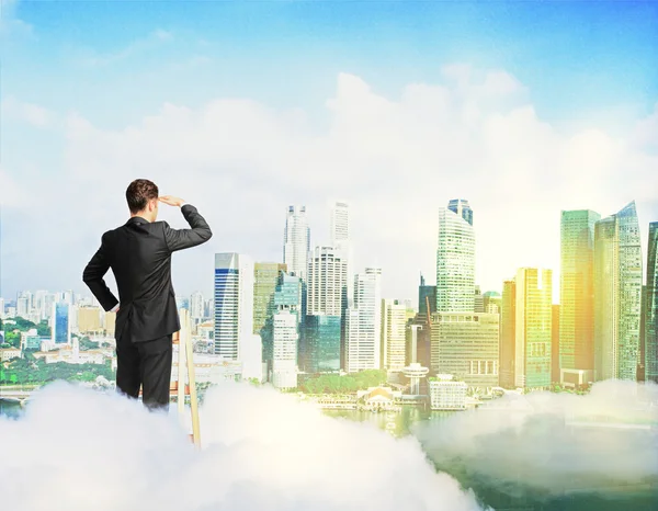 Businessman on ladder above clouds looking into the distance on modern city background with sunlight. Research concept