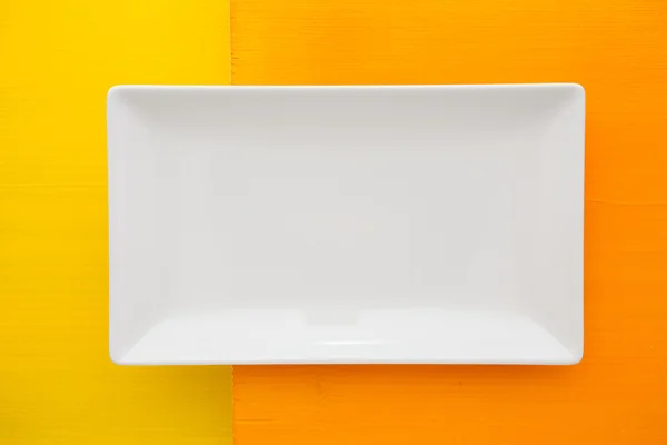 Empty white ceramic dish on over orange  and yellow wooden table