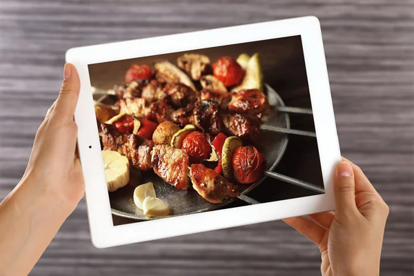 Female hands holding tablet on blurred wooden background. Photo of food on tablet screen.