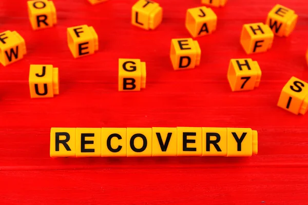 Word recovery made with yellow plastic blocks on wooden background
