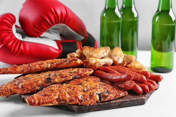 Boxing gloves, snacks and bottles of beer on table against light background