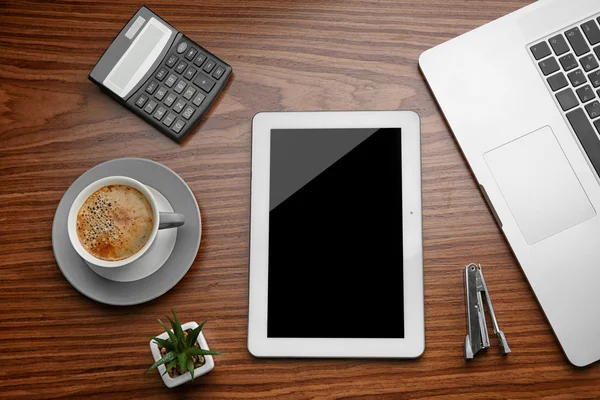 Tablet with cup of coffee and office tools on wooden background