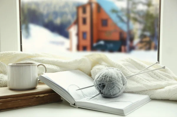 Cup of hot drink and book on the windowsill in winter landscape background