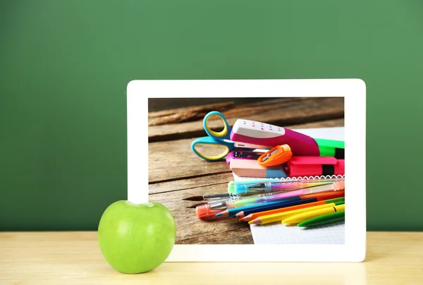 Tablet with stationery wallpaper on screen against chalkboard background. School teacher concept.