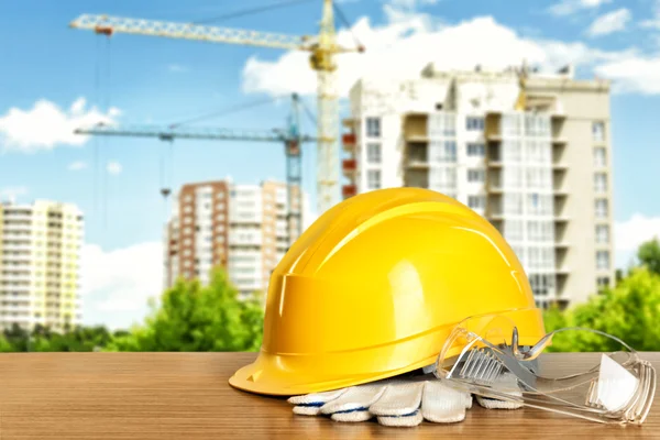 Construction tools and helmet on wooden table and building construction background