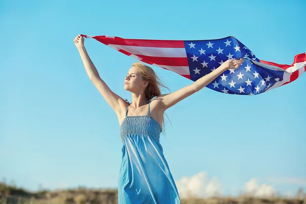 Young woman holding American flag on blue sky background