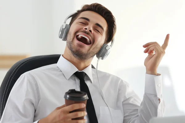 Handsome man singing and listening to music with headphones at work