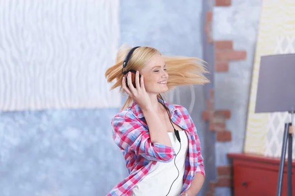 Cheerful girl with headphones listening to music and dancing in the room