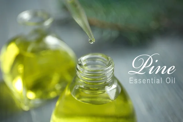 Pipette with essence drop and glass bottle, closeup. Text PINE ESSENTIAL OIL on background. Spa beauty concept.
