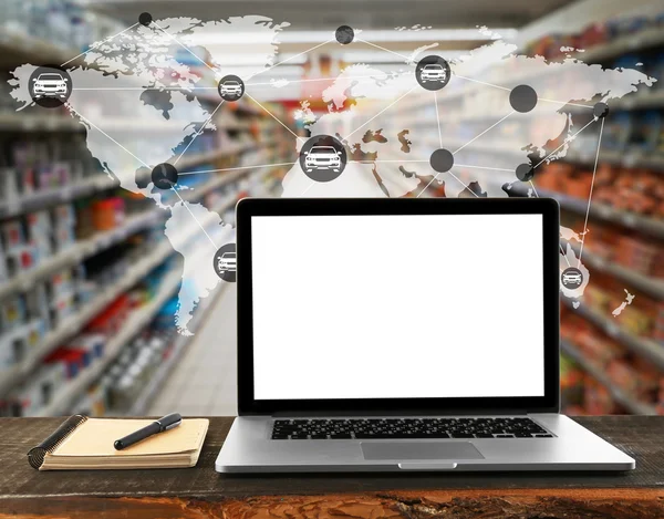 Laptop with blank screen on wooden table. Worldwide transport logistic network on supermarket interior background. Wholesale and retail concept.