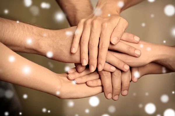 Young people holding hands together, closeup. Snowy effect, Christmas concept.