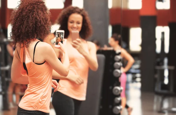 Young sportive woman taking selfie near mirror in gym