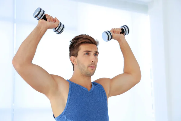 Young man doing exercises with dumb-bells indoors