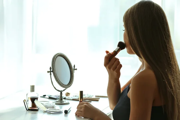 Beautiful young woman looking in mirror while applying makeup