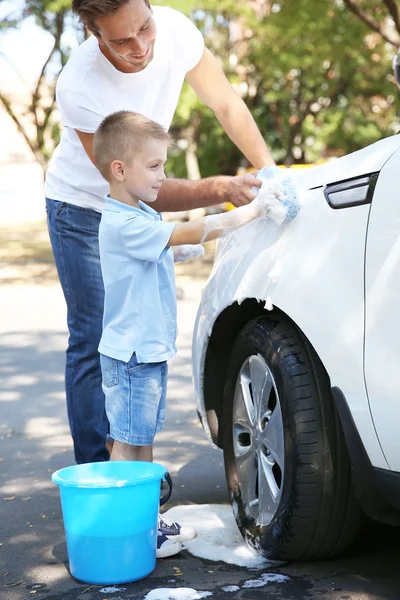 Father and son washing car on street