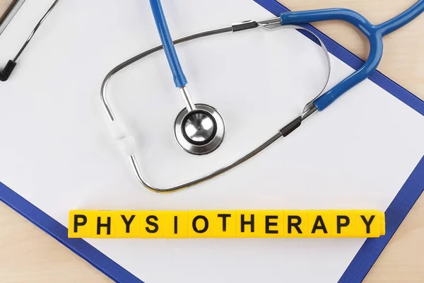 Stethoscope and word PHYSIOTHERAPY made of yellow cubes on clipboard, closeup
