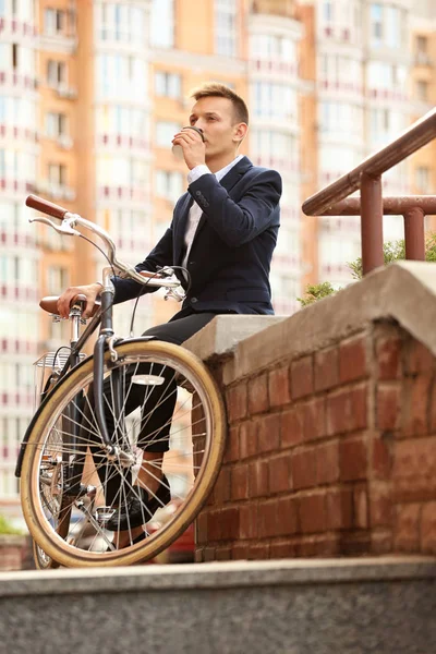 Coffee-to-go concept. Young man with bicycle and cup of coffee on street
