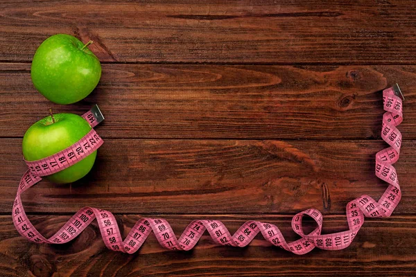 Dieting concept. Green apples with pink measuring tape on wooden background