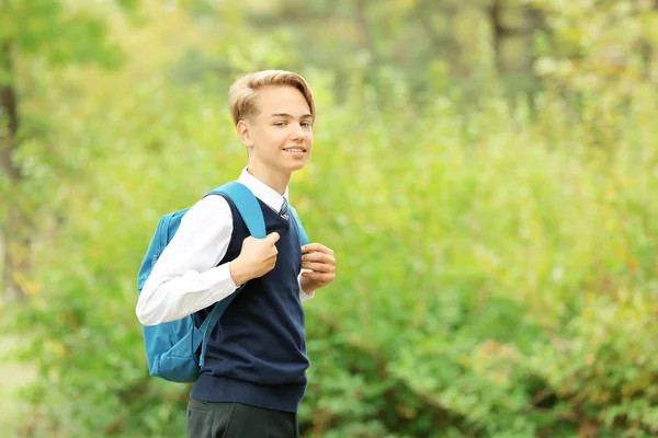 Teenager with bag on green bush