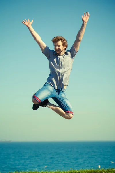 Carefree man jumping by sea ocean water.