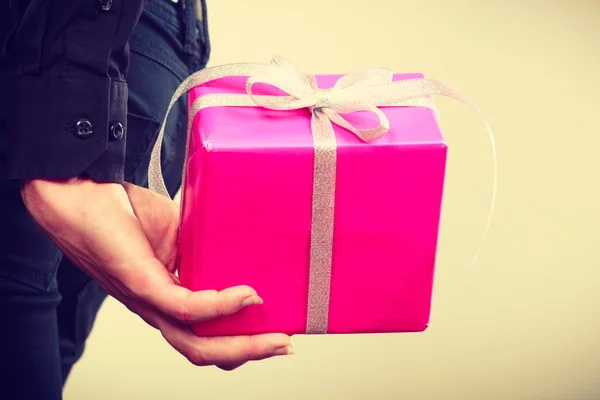 Man hiding pink gift box with ribbon behind back