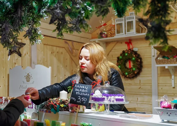 Woman selling handmade soap to customer at Vilnius Christmas Mar