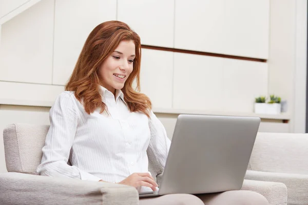 Smiling happy woman sitting on the sofa and using laptop