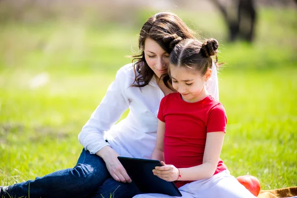 Mother and daughter using digital tablet while sitting in the beautiful nature,