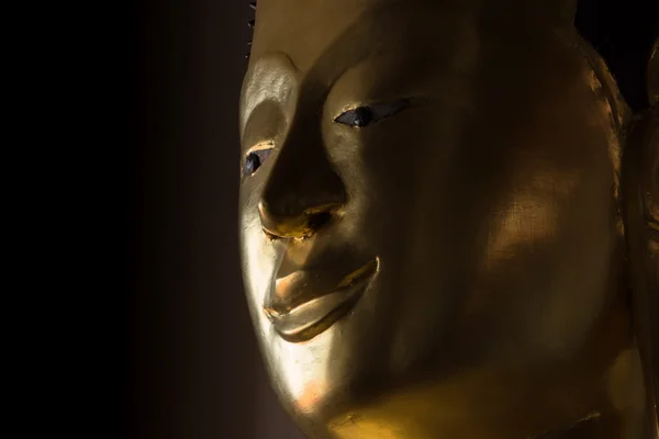 Close up the face of a golden Buddha statue in the dark rooms