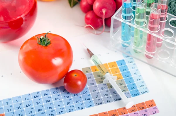 GMO tomatoes, syringe, test tubes in laboratory on periodic table.
