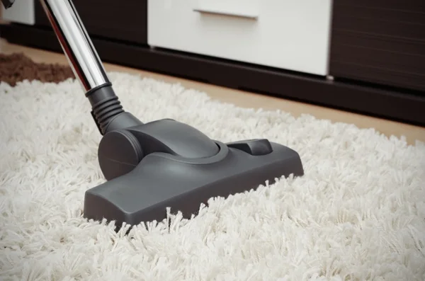 Vacuum cleaner cleans the white shaggy carpet.
