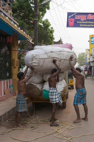 Thee men unload huge cotton bales.