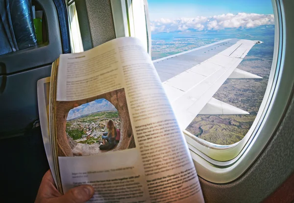 Woman is sitting   by window on a plane with magazine in hands.