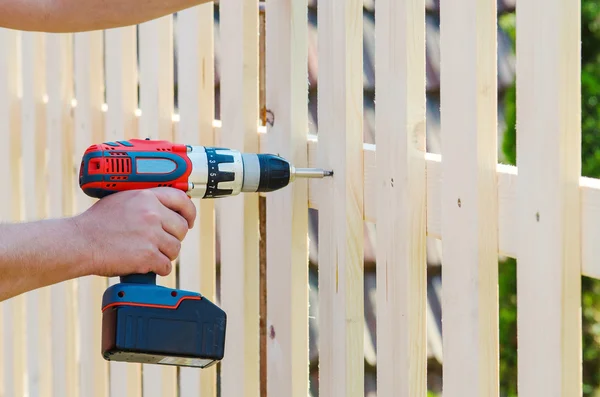 Building a wooden fence with a drill and screw. Close up of his hand and the tool in a DIY concept.