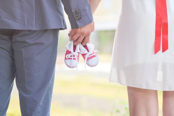 An image of adults holding baby pair of sneakers in red. Pregnancy and expectation.