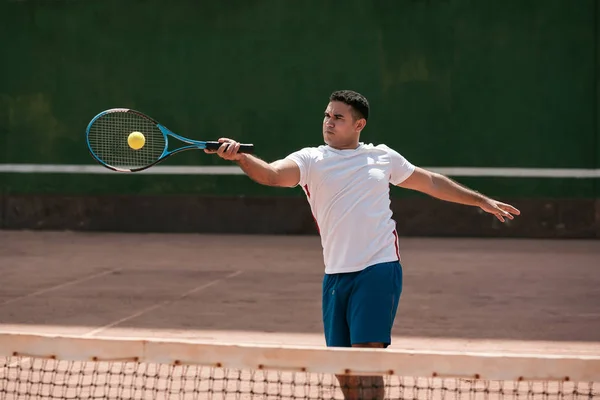 Handsome young man on tennis court. Man playing tennis. Man hitting tennis ball