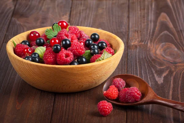 Fresh ripe berries in a wooden plate on the old wooden table. Useful natural food. Fruits and berries