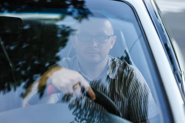 Man with glasses sitting behind the wheel of a car