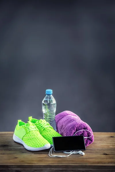 Pair of yellow green sport shoes towel water smart pone and headphones on wooden board. In the background forest or park trail.Accessories for running sport