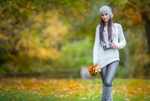 Young attractive brunette woman holding the retro camera in outdoors. Beautiful young girl shooting with retro camera in the autumn sunny day