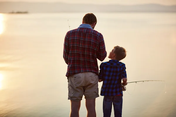Little boy and his father fishing at sunset
