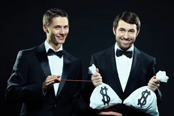 Men in tuxedos holding sacks with money