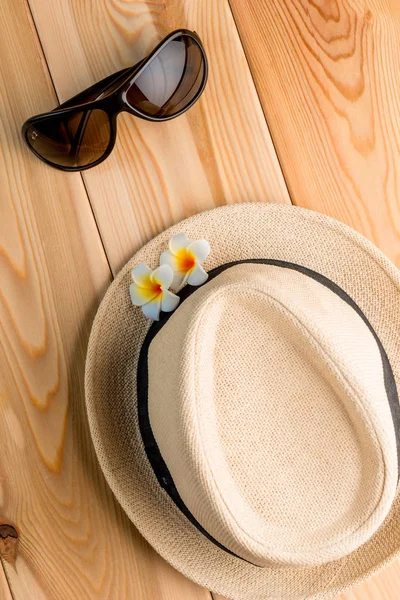 Straw hat and sun glasses on the wooden floor view from above