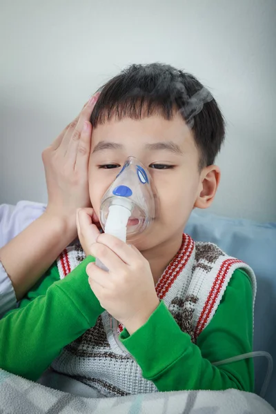 Asian child holds a mask vapor inhaler for treatment of asthma.