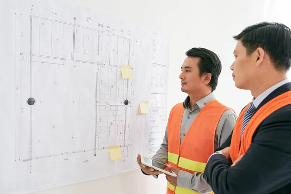 Engineers looking at blueprint on wall